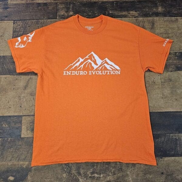 A t-shirt that is orange and has the colorado mountain logo on it.