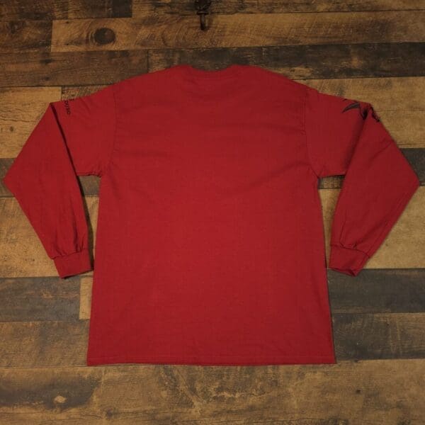 A red long sleeve shirt sitting on top of a wooden floor.